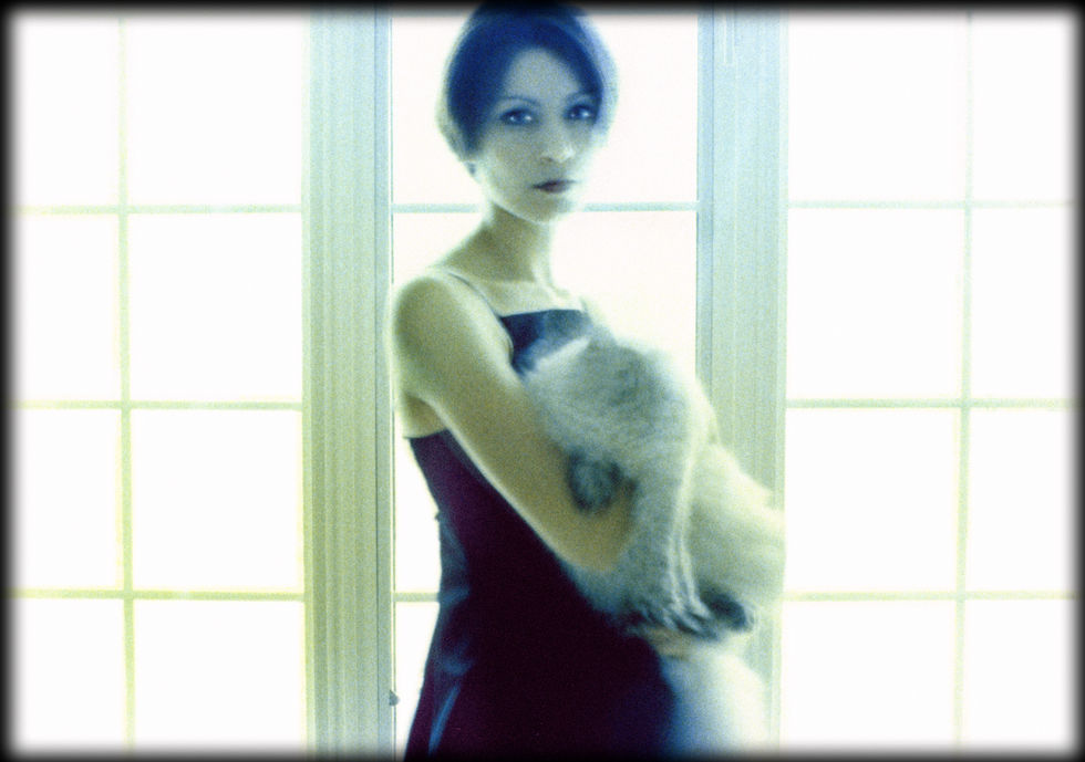 Woman holding fluffy cat by a window.