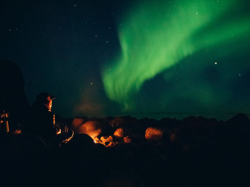 Ung man sitter vid en eld och tittar på norrksen på Lofoten