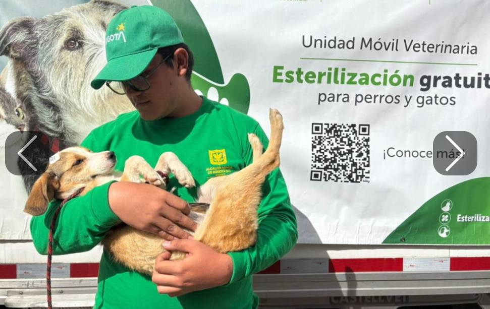 Un hombre alzando a un perro junto a una Unidad Móvil Veterinaria de la ciudad de Bogotá