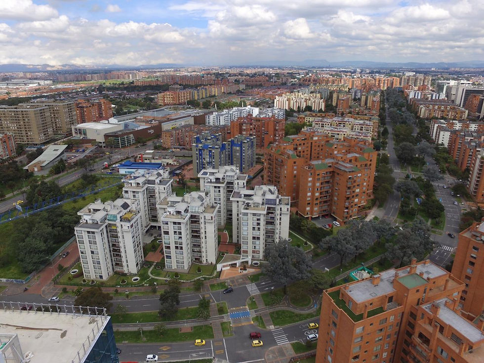 Vista aérea de un barrio urbano con torres residenciales blancas y rojas, avenidas arboladas y cielo nublado.
