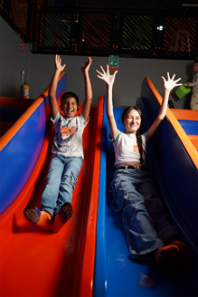 Un niño y una niña jugando en un tobogán de un parque de diversiones bajo techo