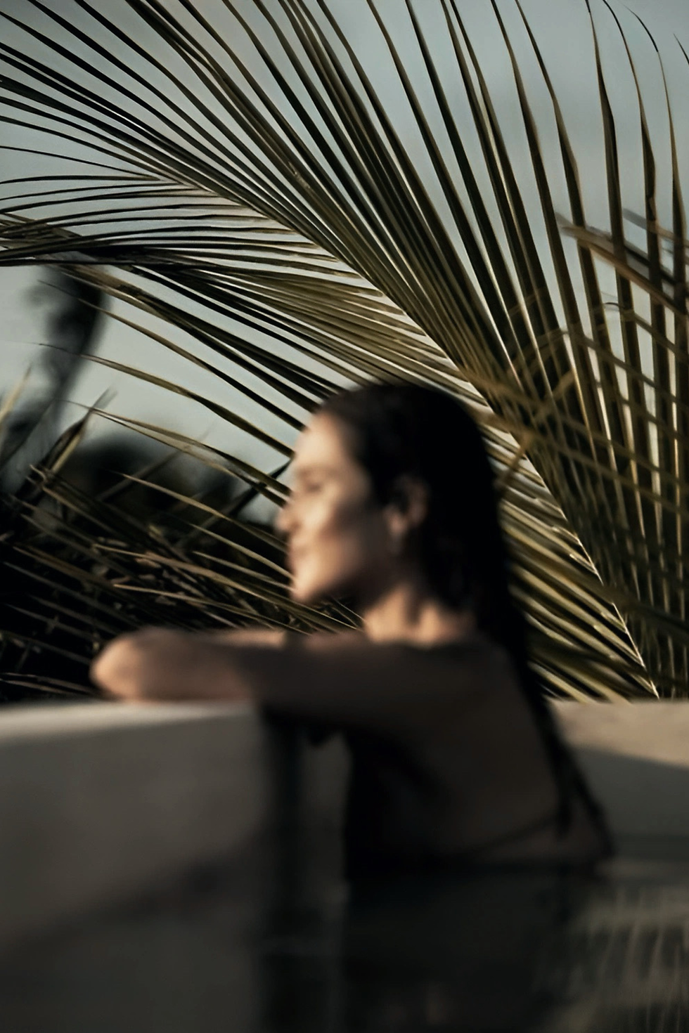 Aerial view of a marina with yachts and sailboats docked, surrounded by a rocky shore. Buildings and greenery in the background under a clear sky.