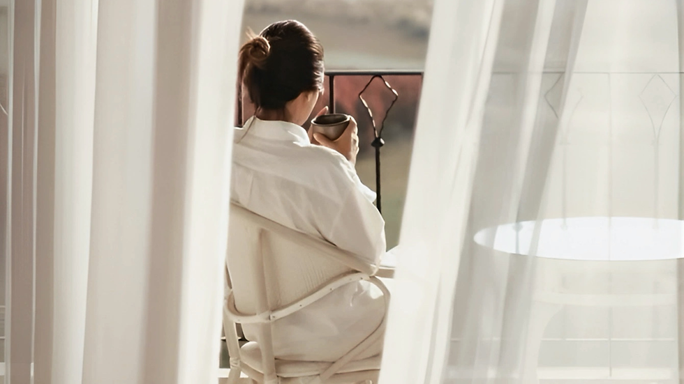 Aerial view of a marina with yachts and sailboats docked, surrounded by a rocky shore. Buildings and greenery in the background under a clear sky.