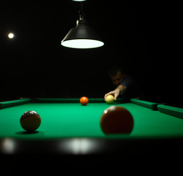CLOSE IN BILLIARDS SHOT WITH TABLE LIGHT ABOVE AND DARK BACKGROUND ADD A PERSON SHOOTING A