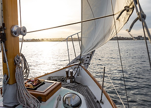 image looking forward at the bow of a sailboat and the dark blue water beyond, the jib is filled with wind.