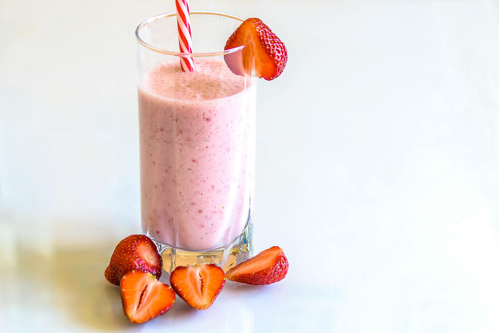 A pink strawberry smoothie in a glass cup with cut strawberries in front of the smoothie