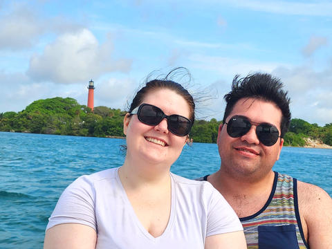 A couple is taking a photograph while on the Bonnie Lee with the historic Jupiter lighthouse in the background at the Jupiter Florida Inlet