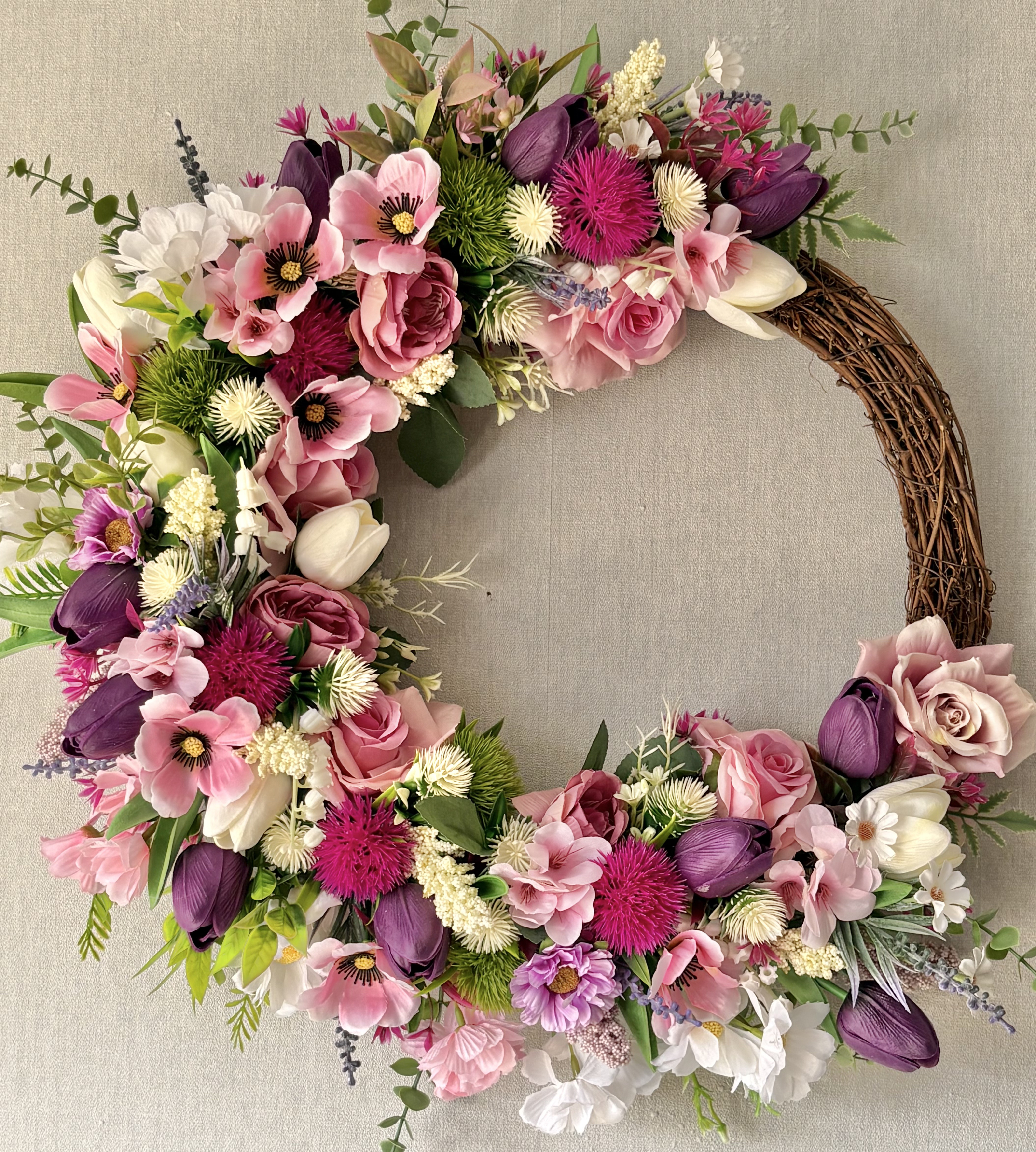 A beautifully handcrafted artificial floral summer wreath hanging elegantly on a rustic wooden door in the bright July sunshine.
