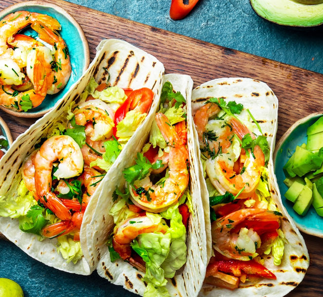 Tacos gefüllt mit Garnelen, Avocado, Salat auf Holzbrett.