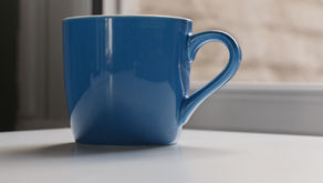 A blue mug of tea, made by a human, sits on a white desk in front of a window