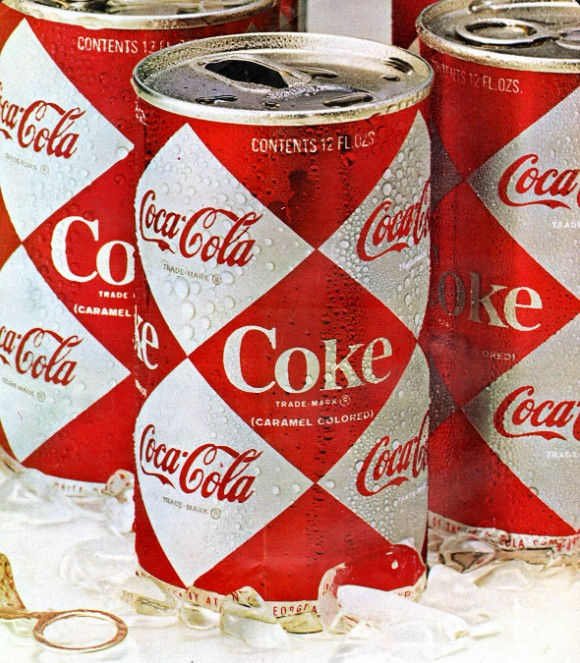 Cans of Coke with red and white diamond pattern, covered in condensation, standing on a white surface with pull tabs. Retro design.