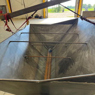 Interior view of a custom fabricated steel hopper showing tapered sidewalls, internal support bars, and a center discharge outlet designed for efficient bulk material flow.