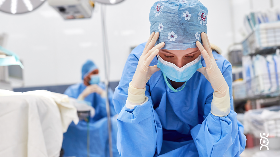 Personal médico en quirófano. Una doctora con uniforme azul y gorro floral se sostiene la cabeza, el ambiente es tenso y concentrado.