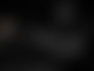 Ultrarealistisches Schwarz-Weißfoto eines taktischen Stressdrills: Einsatzkraft in Schutzweste, Gehörschutz und Schutzbrille feuert eine Pistole im beidhändigen Anschlag auf dem Indoor-Schießstand; Mündungsfeuer und ausgeworfene Patronenhülse sind eingefroren, im Hintergrund unscharfe Ziele sichtbar, dramatische Beleuchtung