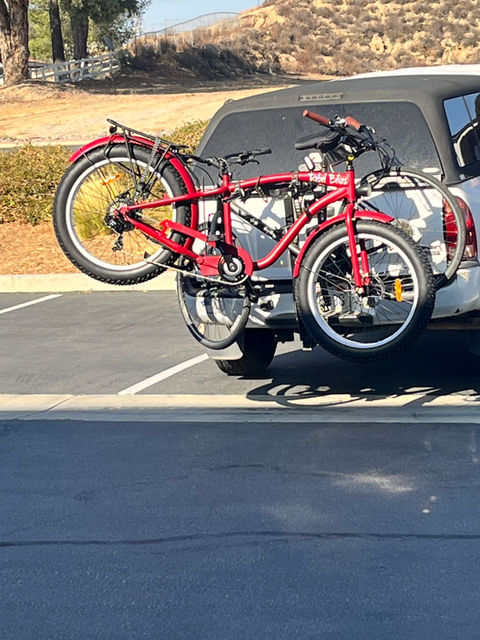 Red e-mountain bike on car rack in sunny lot.