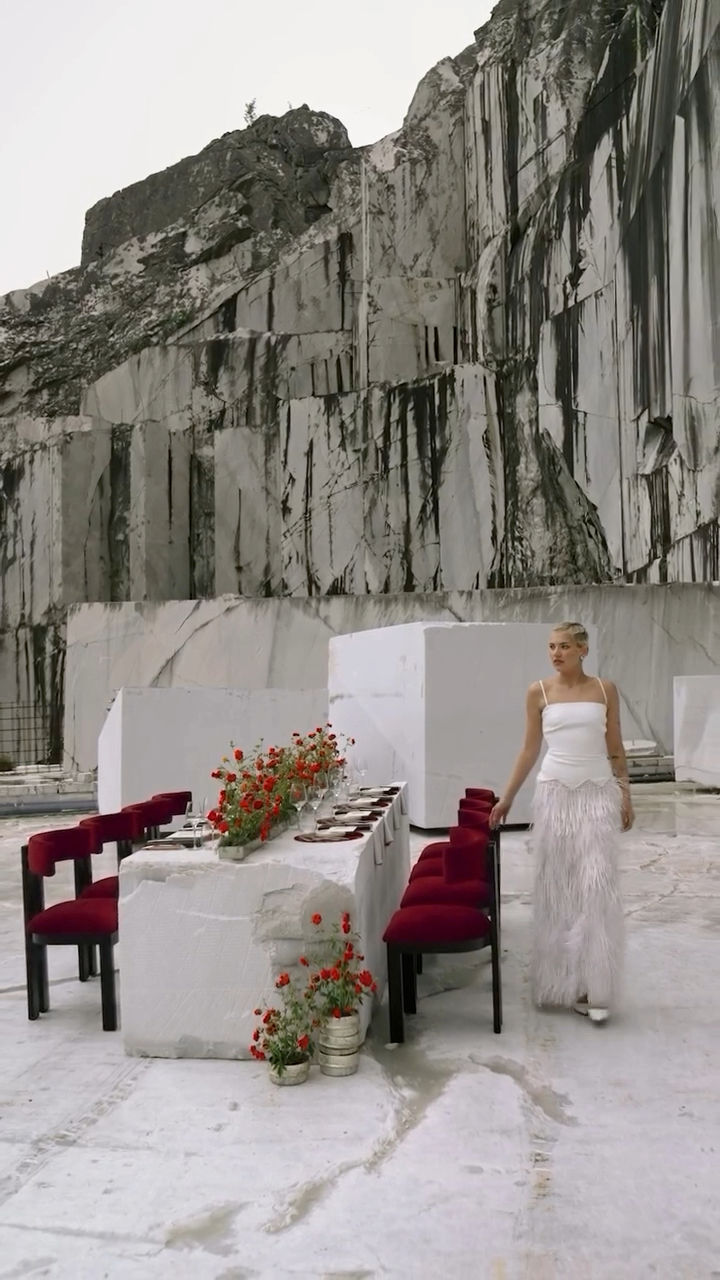 A blond girls dress in withe to celebrate life in a stunning landscape with marble mountain and beautiful table with red chairs and red flowers.