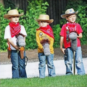 "Three Children riding Stick Horses, Wearing Red Bandannas and Country Hats, Engaging in Playful Thematic Birthday Party."