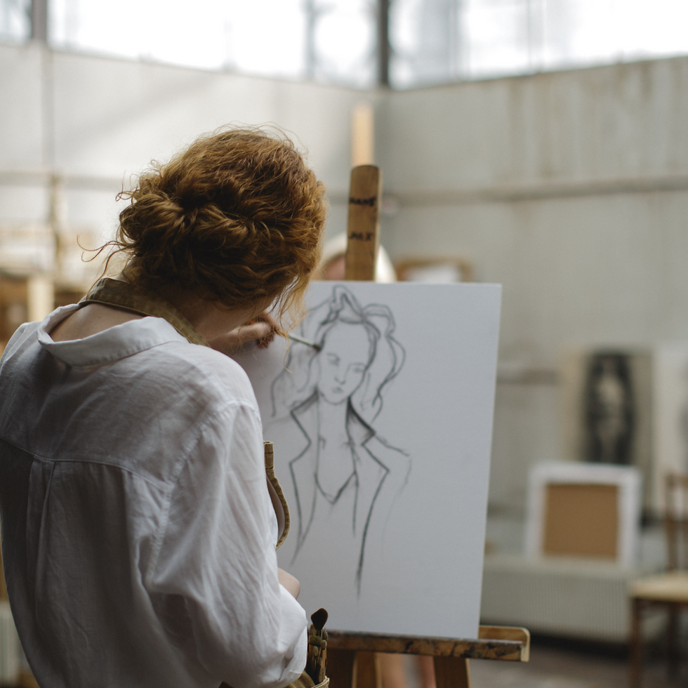 Artist sketching a portrait on canvas in a well-lit studio. She has red hair and wears a white shirt. The mood is focused and creative.