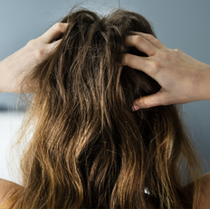 Person with long brown hair holds their head with both hands, set against a blurred gray and white background, conveying stress or frustration.