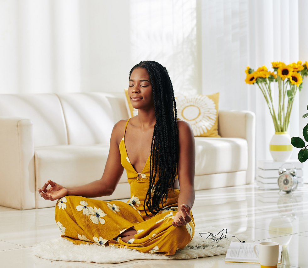 Woman meditating on floor in yellow floral dress, eyes closed. Calm room with sunflowers, cream sofa, book, and clock in background.
