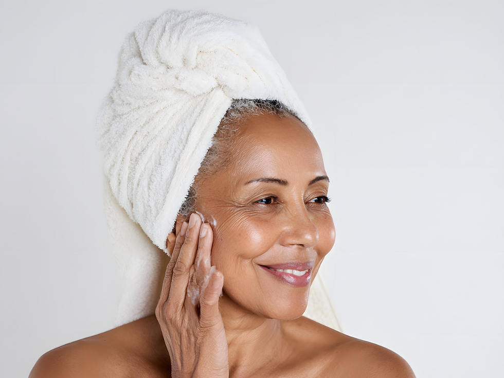 Woman with a towel on her head smiles gently, touching her face. White background; serene and content mood. No visible text.