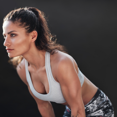 Woman in activewear leans forward with focused expression against a dark background. She's wearing a gray sports bra and patterned leggings.