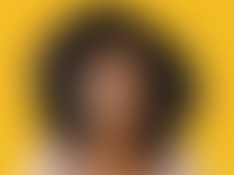 Woman with curly hair and glasses showing a thoughtful expression against a bright yellow background. Wearing a striped top.