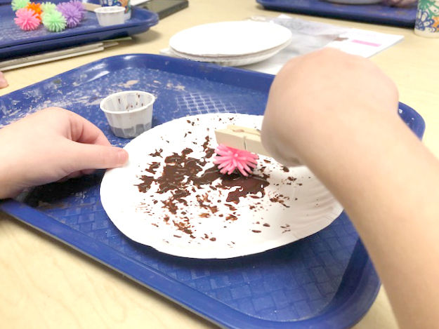 child painting on paper plate using pokey ball and clothepin