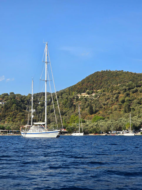 Un yacht blanc ancré dans la mer bleue, devant une colline verdoyante