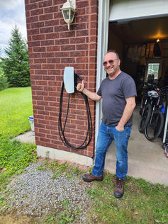 Un homme souriant montre une borne de recharge pour véhicule électrique. PhidelÉlectrique.ca