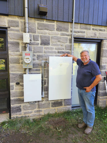 Homme pose avec un boîtier blanc, mur de briques, PhidelÉlectrique.ca