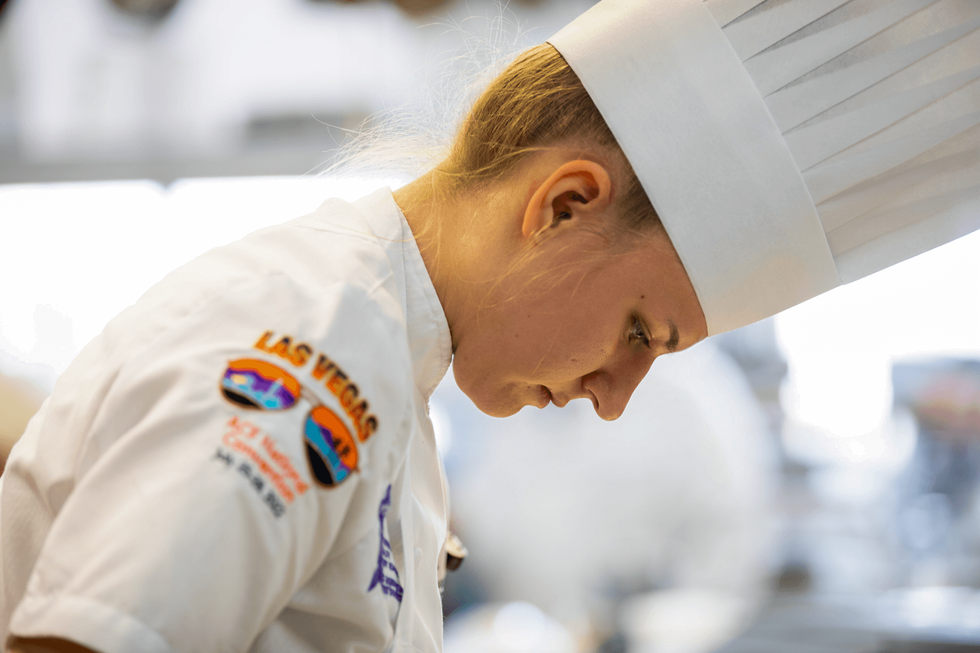 A bakery student leans over her work.
