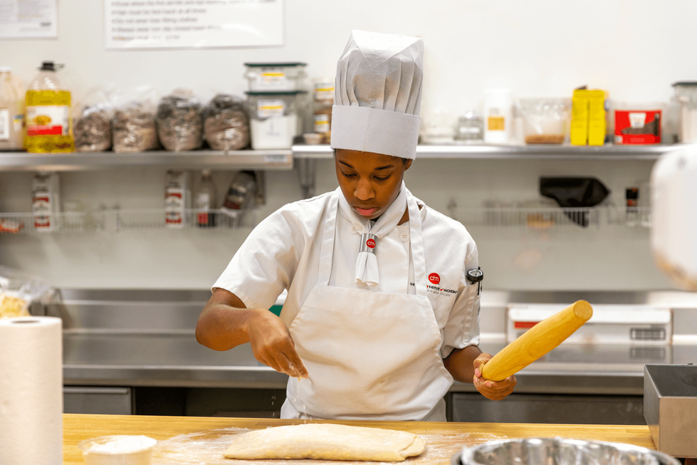 A baking student sprinkles flour on her table.