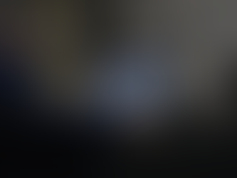 Man in cap works at desk, viewing bill of lading on monitor. Printers and shelves visible. Office setting, dim lighting.