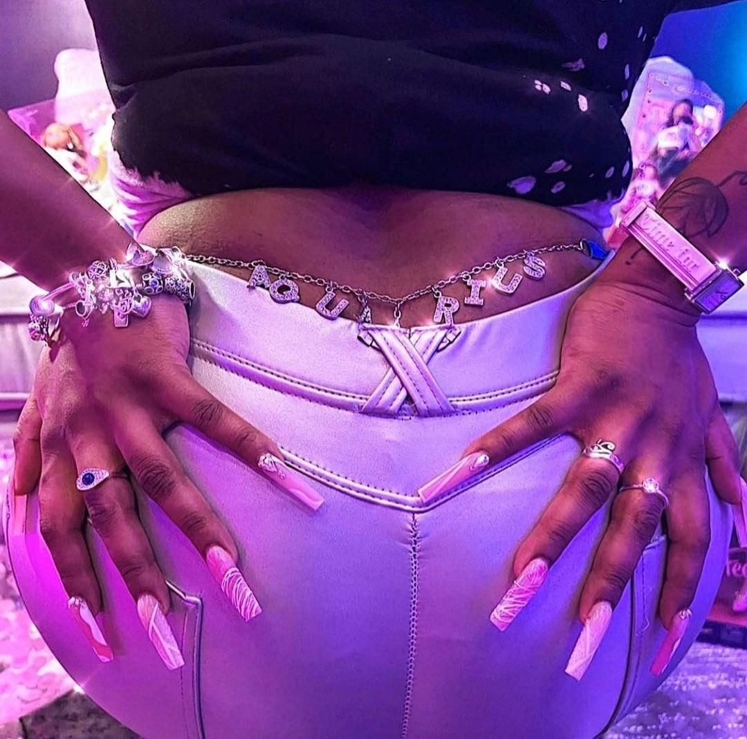 Model with long statement nails and jewelry, showcasing a stylish and cosmic vibe while wearing a rhinestone Aquarius thong