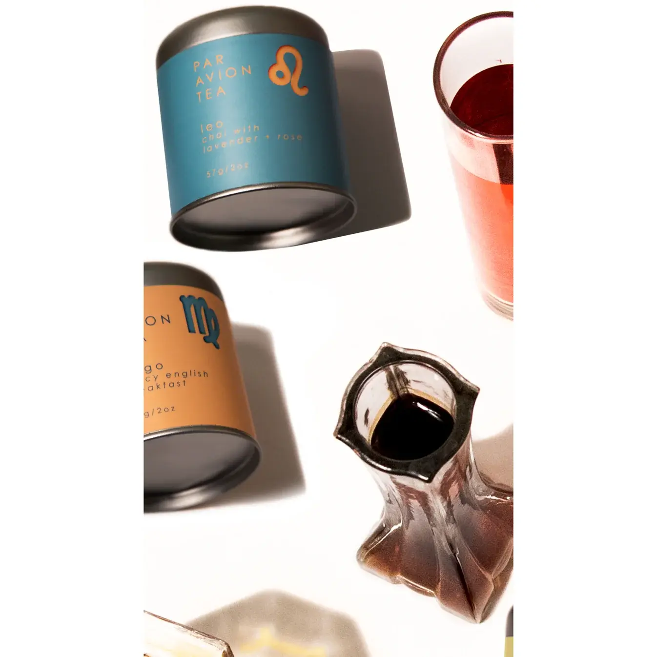Flat lay of Leo Luxury Zodiac Tea canister styled with other zodiac blends and a glass of brewed tea