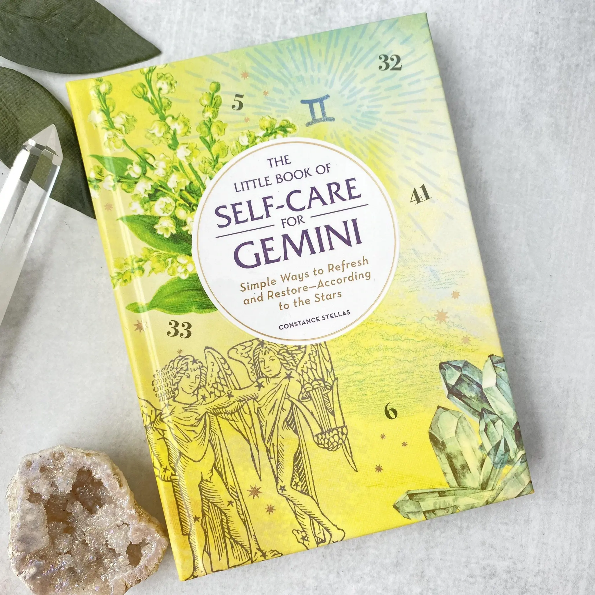Flat lay of the Gemini self-care book front cover on a white background, styled with a white crystal and clear quartz point