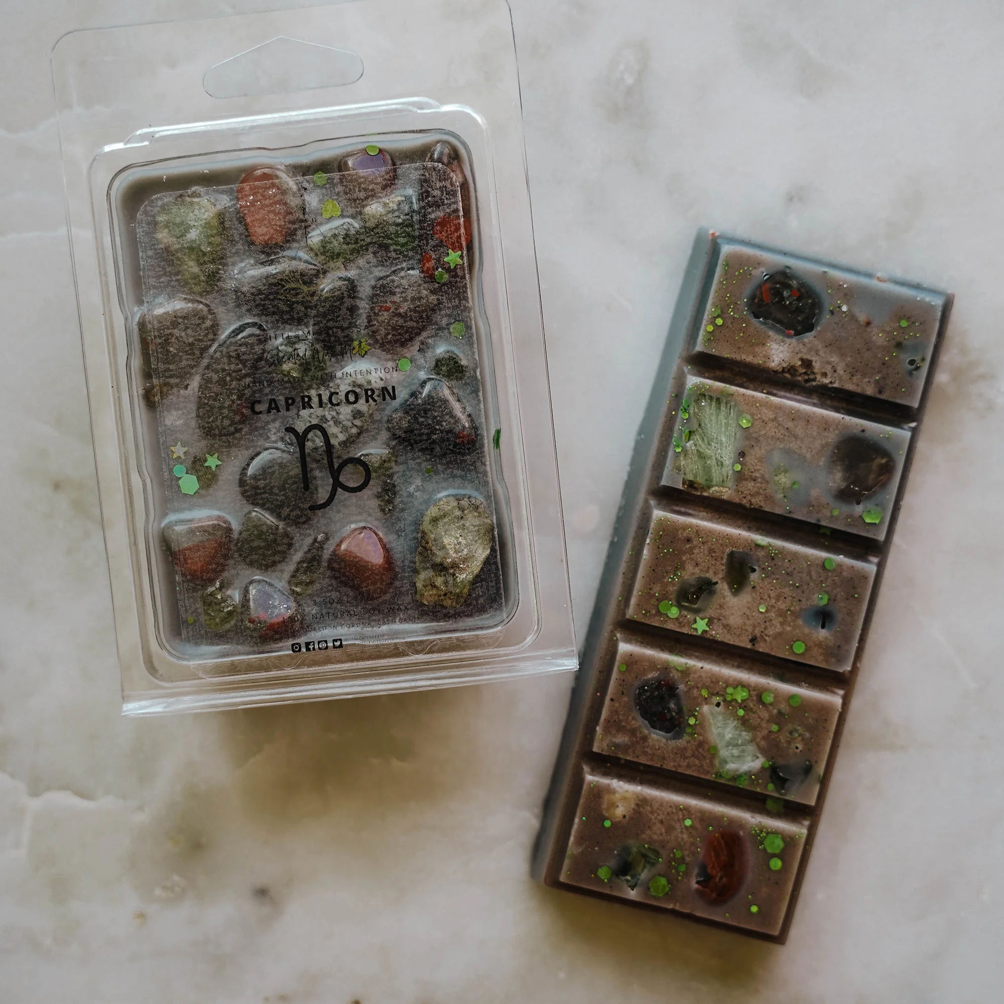 Capricorn zodiac wax melt and snap bar in earthy brown and black tones with crystals, displayed on cream marble surface