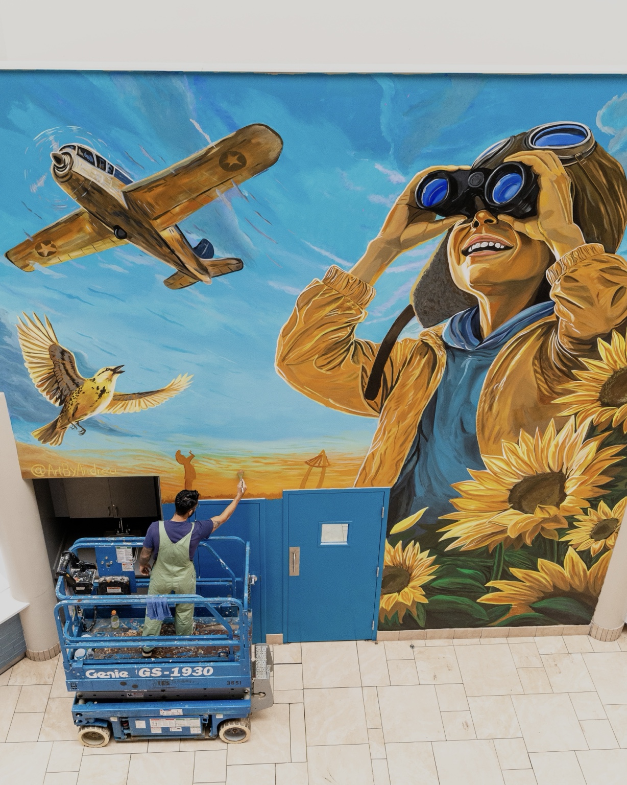 Wide view of the Towne East Square aviation mural showing the full wall, lift, and artist during installation