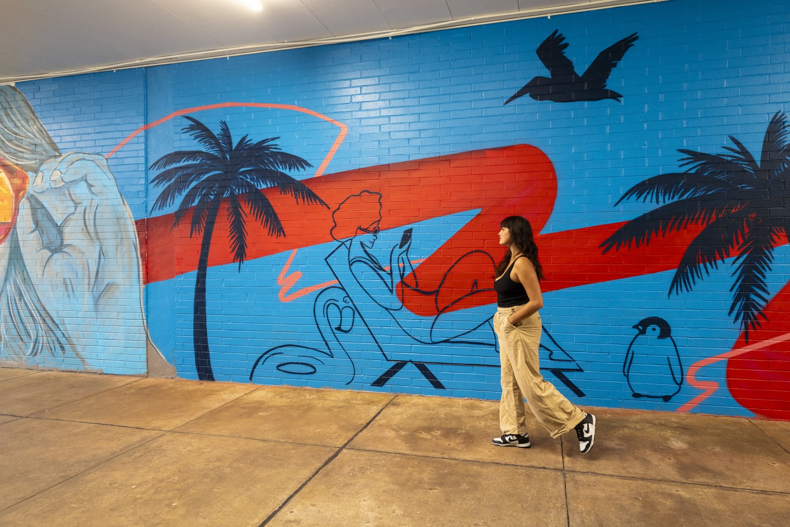 Pedestrian walking past a Pensacola-themed mural with palm trees and coastal imagery