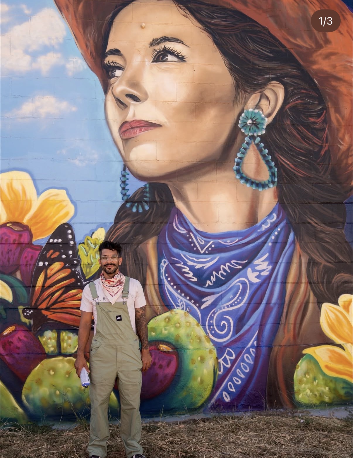 Artist standing in front of detailed cowgirl mural with turquoise earrings, blue bandana, butterflies and desert flowers
