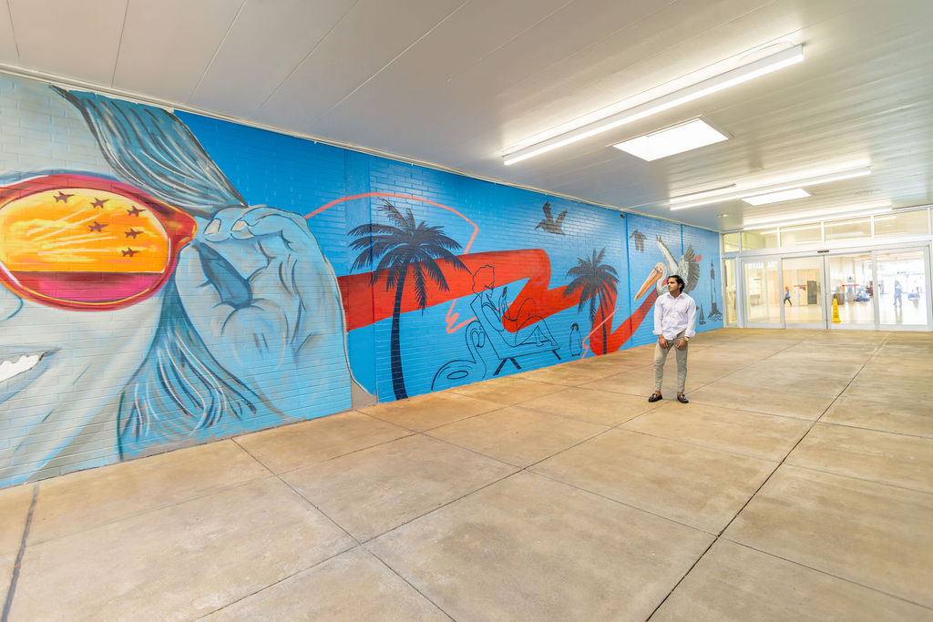 Wide view of the 120-foot Cordova Mall pedestrian tunnel with a Pensacola-themed mural of aviation, palm trees, and coastal imagery
