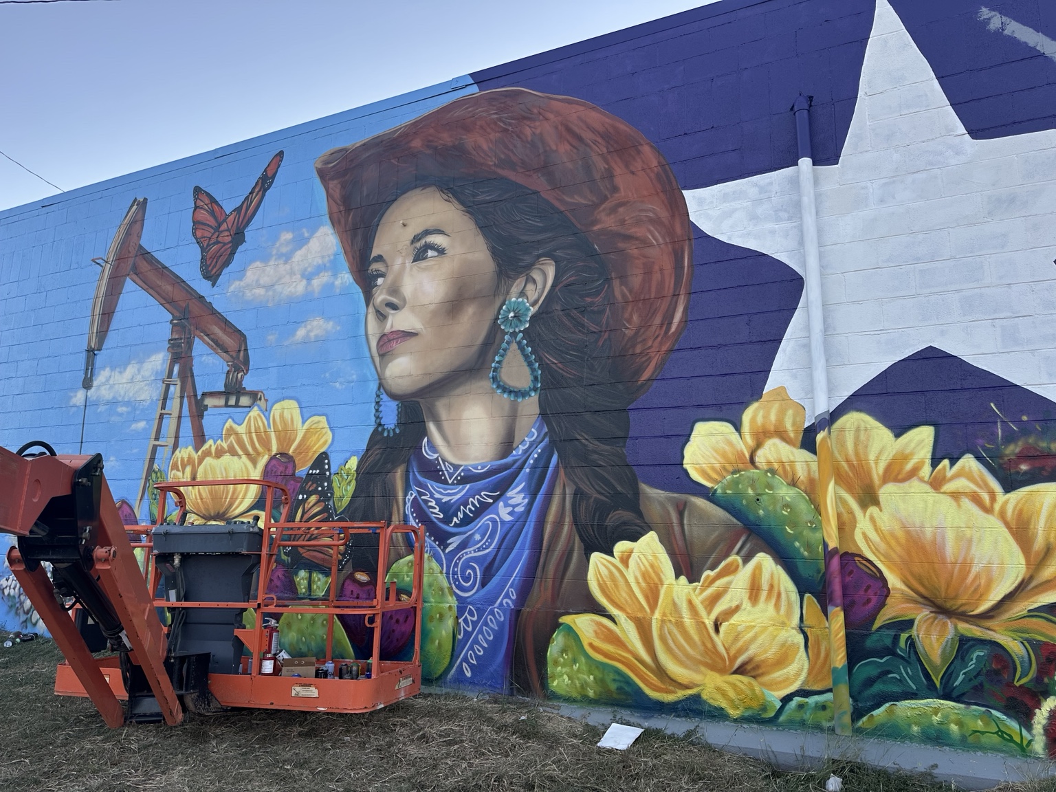 Wide view of the Western mural in Snyder Texas, featuring a cowgirl portrait, pumpjack, butterflies and flowering cacti
