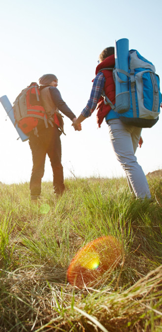 A couple walking through a golden field with backpacks, symbolizing support and partnership on the path to resilience.