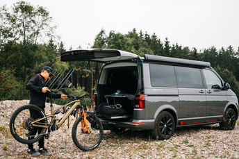 VW T6.1 mit vertikalem Fahrradträger. VW Bus, oder Kleinbus wie Mercedes Viano oder V-Klasse. Ein Mann repariert ein Conway E-Bike an dem MOTUS Fahrradträger.