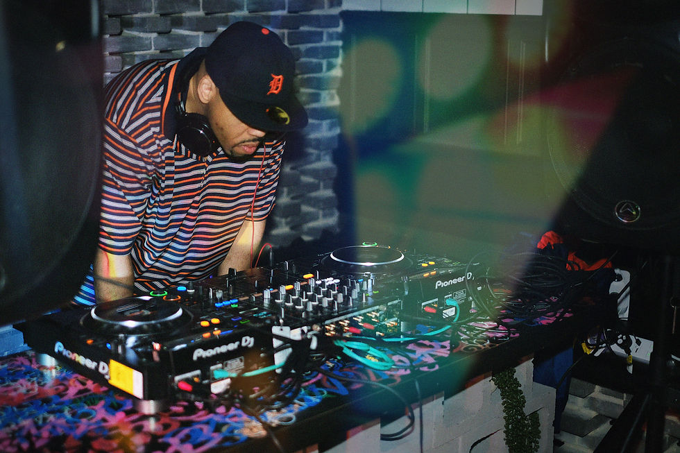 DJ in striped shirt mixes at a colorful graffiti-covered booth. Brick wall background, vibrant lights, focused mood. Equipment labeled "Pioneer DJ."
