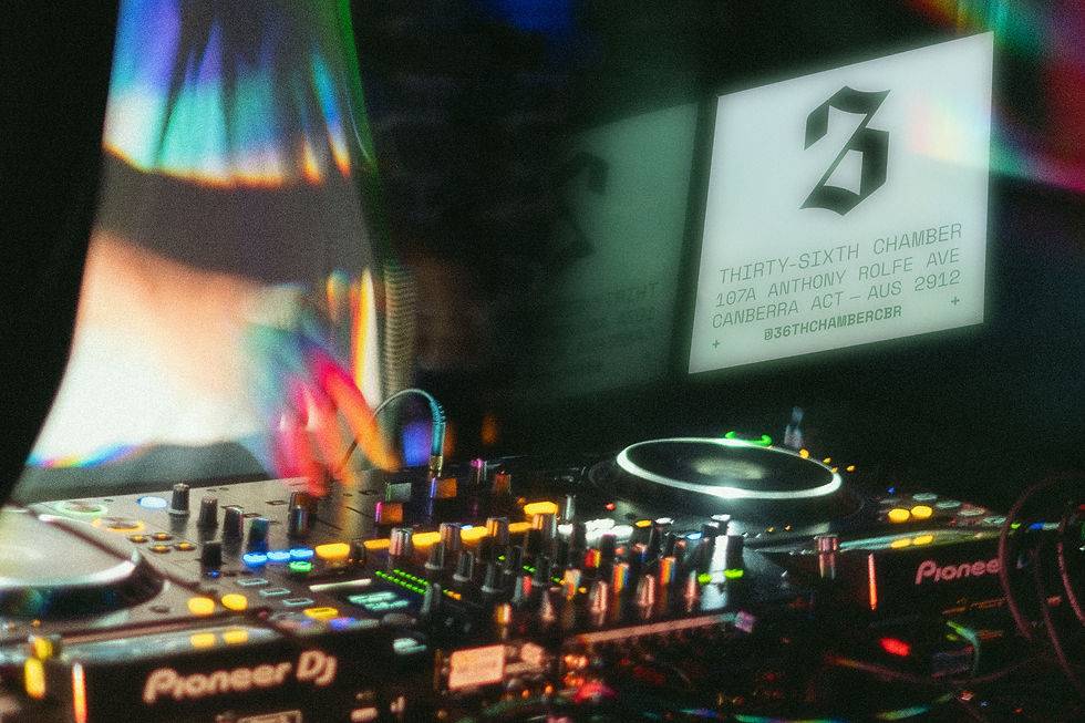 DJ booth with colorful lights reflecting on equipment. Sign reads "Thirty-Sixth Chamber, 107A Anthony Rolfe Ave, Canberra ACT." Energetic vibe.