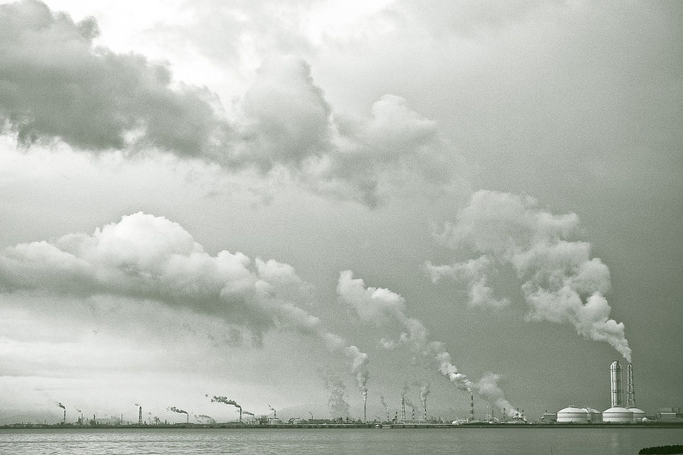 Plumes of emissions billow out from a series of smokestacks and towers from an industrial waterfront facility.