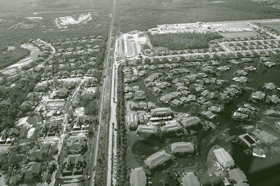 An aerial view depicts damage from Hurricane Ian. The picture shows one neighborhood with houses completely submerged by water with only rooftops showing while across a highway, another community is untouched by floodwaters.