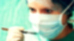 Surgeon in blue scrubs and mask holds a scalpel, focused expression. Green surgical background.